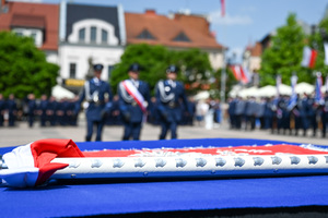 kolorowe zdjęcie przedstawiające sztandar, w tle umundurowani policjanci