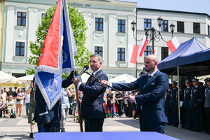 kolorowe zdjęcie przedstawiające mężczyznę w garniturze, który trzymając sztandar prowadzi przemówienie