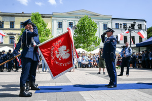 kolorowe zdjęcie przedstawiające Oficera Policji oddającego honor do sztandaru trzymanego przez innych policjantów