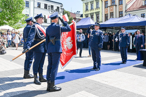kolorowe zdjęcie przedstawiające Oficera Policji oddającego honor do sztandaru trzymanego przez innych policjantów