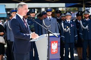 kolorowe zdjęcie przedstawiające mężczyznę w garniturze  podczas przemówienia, w tle policjanci oraz goście honorowi obchodów Święta Policji