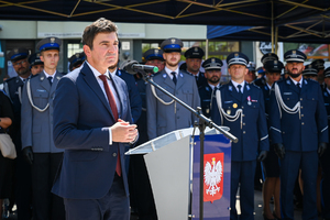 kolorowe zdjęcie przedstawiające mężczyznę w garniturze  podczas przemówienia, w tle policjanci oraz goście honorowi obchodów Święta Policji