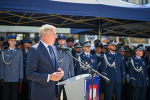 kolorowe zdjęcie przedstawiające mężczyznę w garniturze  podczas przemówienia, w tle policjanci oraz goście honorowi obchodów Święta Policji