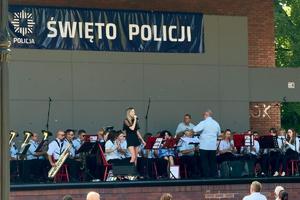kolorowe zdjęcie przedstawiające scenę na której znajduje się kobieta z mikrofonem i orkiestrą, nad sceną widoczny napis Święto Policji