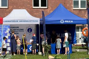 Kolorowe zdjęcie przedstawiające namiot promocyjny Policji oraz Laboratorium Kryminalistyki, widać umundurowanych policjantów, dzieci oraz osoby dorosłe.