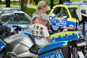 Kolorowe zdjęcie przedstawiające dzieci, które siedzą na motocyklach policyjnych. W tle widoczne są radiowozy policyjne.