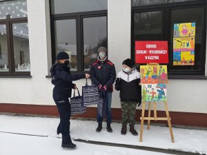 Policjant wręcza nagrody uczniom z Ośrodka Szkolno-Wychowawczego w Kaczynie, przed budynkiem placówki