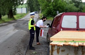 policjantka i pracownica PKP wręczające kierowcy ulotkę, w tle przejazd kolejowy