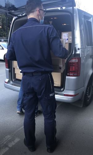 policjant wnosi kartonowe pudła do radiowozu