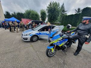 Samochód oraz motocykl policyjny stojący obok siebie, przy motocyklu stoi policjant