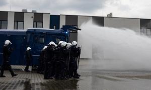 Szyk policjantów, armatka wodna wypuszcza wodę przez dysze
