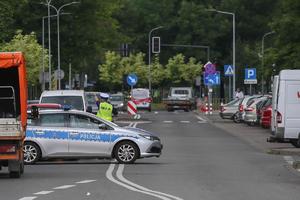 policjant ruchu drogowego stojący przed radiowozem na jednej z krakowskich ulic wskazuje kierunek kierowcy samochodu