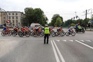 policjant ruchu drogowego zabezpieczający trasę zawodów triathlonu w trakcie przejazdu kolarzy przez jedną z ulic