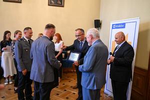 dwóch policjantów w trakcie odbierania nagrody ,,Bezpieczny Kraków&#039;&#039; od krakowskich urzędników