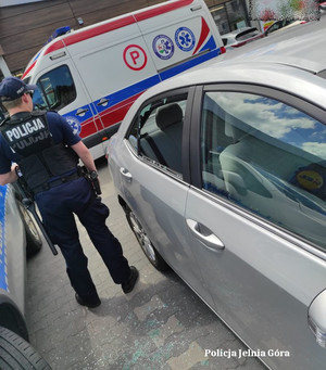 policjant stojący obok samochodu z wybitą szybą, w tle widać karetkę i radiowóz obok