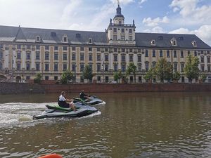 umundurowany funkcjonariusz policji pływający na skuterze wodnym, w tle budynek uniwersytetu wrocławskiego