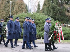 Policjanci w mundurach galowych niosą wieniec pogrzebowy