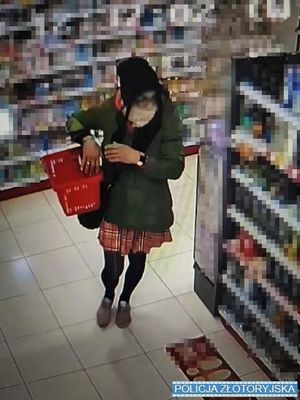 Zdjęcie z kamery sklepowej przedstawiające mężczyznę przebranego za kobietę, ubranego w płaszcz, spódnicę, okulary i czapkę, trzymającego w ręku koszyk sklepowy, przechodzącego pomiędzy regałami sklepowymi.