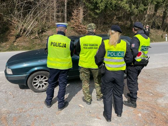 Na dworze stojące przy drodze osoby w kamizelkach odblaskowych