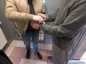 Na zdjęciu policjant zakłada kajdanki zatrzymanemu.
