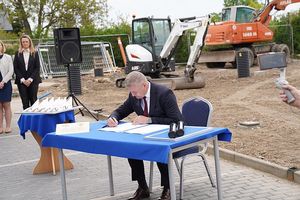 Na zdjęciu Wójt Gminy Męcinka Pan Mirosław Brzozowski podpisujący akt erekcyjny, w tle plac budowy z maszynami budowlanymi.