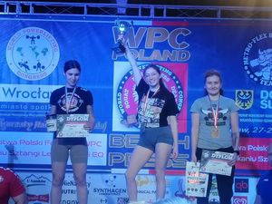 Na zdjęciu trzy kobiety stojące na podium z medalami i pucharami.