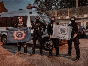 Umundurowani policjanci na tle oznakowanego radiowozu