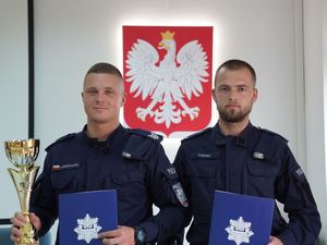 Dwaj policjanci z dyplomami i pucharem. W tle godło Polski.