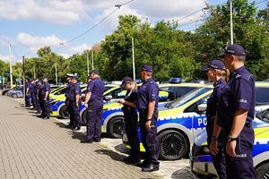 policjanci stojący na dworze przy oznakowanych radiowozach