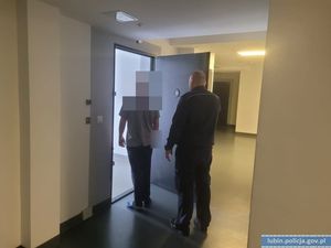 Policjant i osoba w szarej koszulce przed drzwiami w pomieszczeniu
