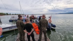 Policjanci na nadbrzeżu przy łodziach instruują żołnierzy jak przygotować sprzęt do radowania tonącej osoby.