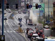 Widok z kamery miejskiej na zatłoczoną ulicę i policjanta gaszącego płonący samochód