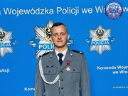 Policjant w mundurze pozujący do zdjęcia na banerze Komendy Powiatowej Policji w Oławie
