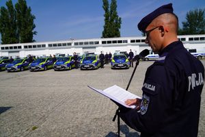 policjant czyta coś z kartki - w tle nowe radiowozy