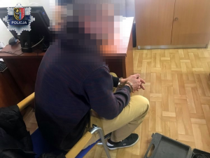 Na zdjęciu zatrzymany mężczyzna, który siedzi na fotelu z kajdankami na rękach