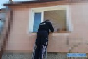 Na zdjęciu widać jak policjant stoi na drabinie aby wejść przez okno do mieszkania gdzie kobieta potrzebowała pomocy