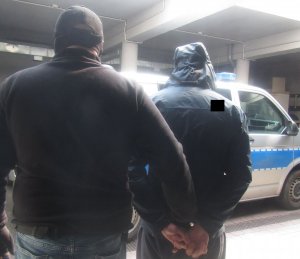 nie umundurowany policjant stoi koło radiowozu z zatrzymanym mężczyzną