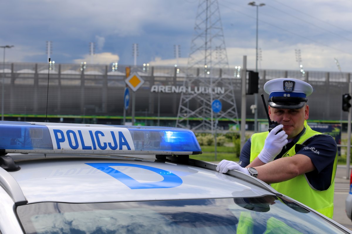 policjant przy radiowozie przed stadionem w ręku trzyma radiostacje