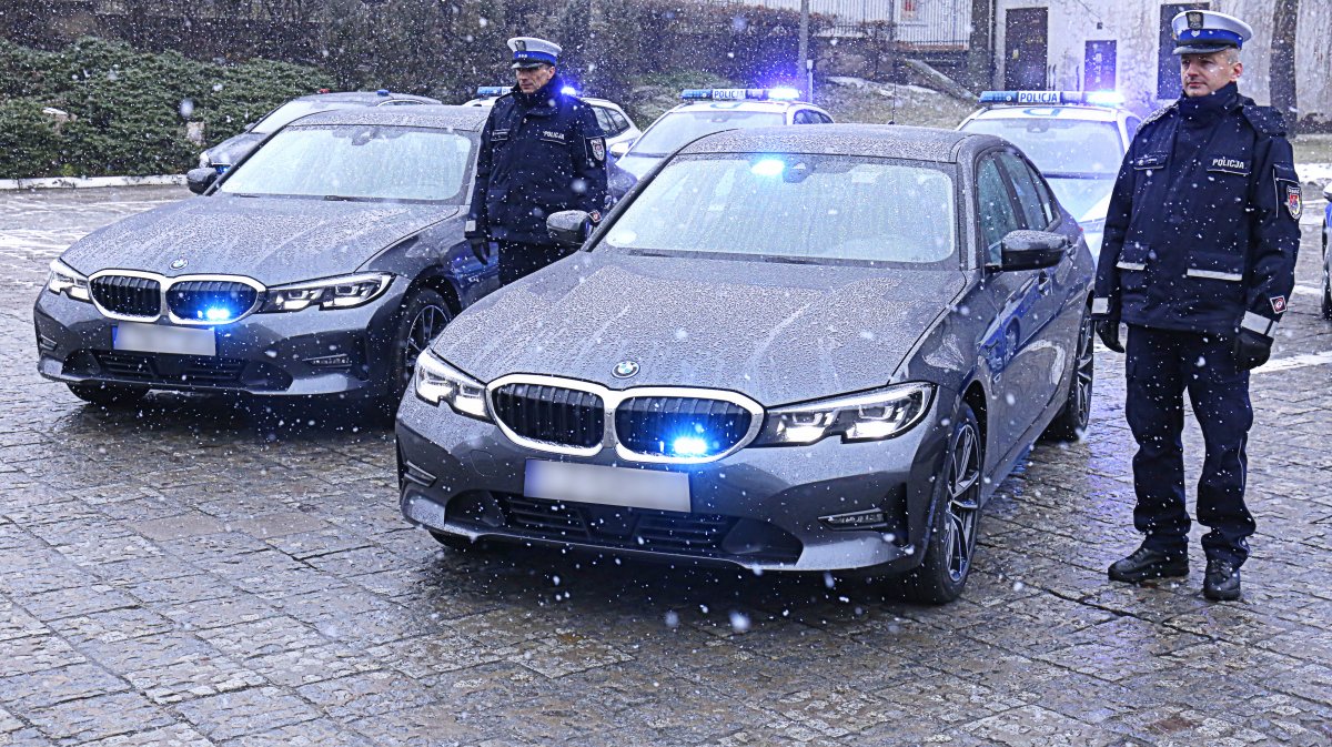 Dwa nowe radiowozy nieoznakowane BMW przy których stoją policjanci.