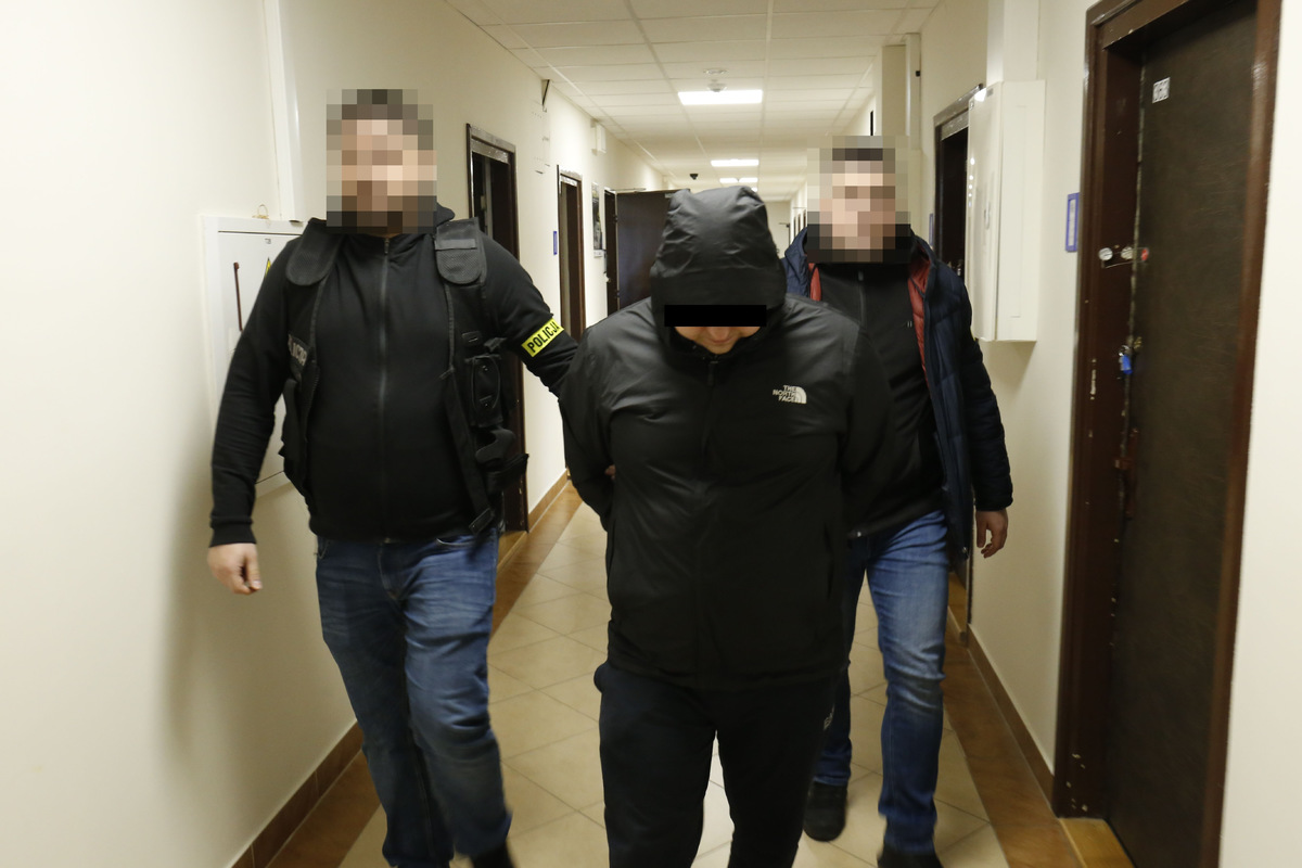 Policjanci prowadzą zatrzymanego mężczyznę w Komendzie Wojewódzkiej Policji w Lublinie.