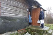 starsza kobieta otwierająca drzwi domu oraz policjant i przedstawicielka GOK w Milejowie przekazujący paczki świąteczne