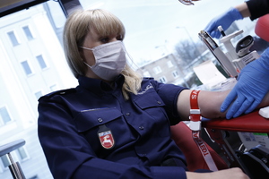 Policjantka ubrana w mundur z napisami policja oddaje krew w mobilnym punkcie.