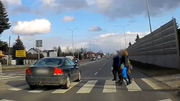 Stop klatka z filmu na którym widać jak osobowe auto przejeżdża przez przejście dla pieszych w chwili gdy znajdują się na nim piesi.