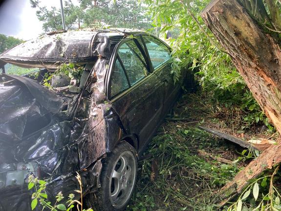 Pojazd Honda po wypadku pod drzewem. W tle policjant