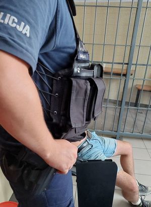 policjant pilnuje siedzącego zatrzymanego