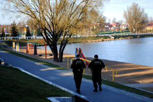 Patrol policji idzie wzdłuż zalewu i placu zabaw.