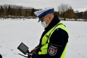 Policjant patrzy na ekran urządzenia rejestrującego lot drona.