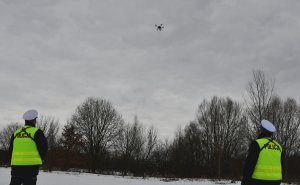 Policjanci patrzą się w górę w kierunku latającego drona.