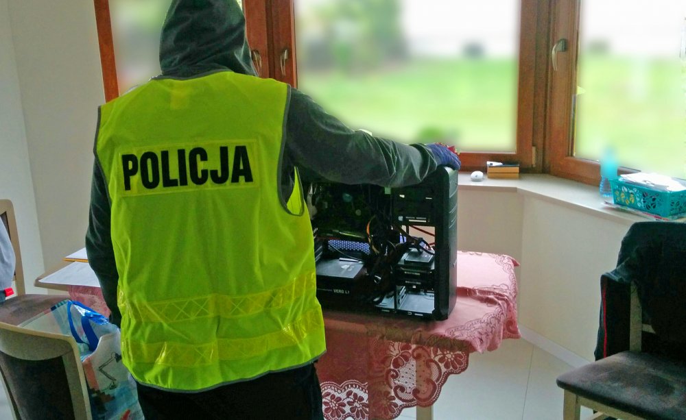 policjant w żółtej kamizelce z napisem Policja i zabezpieczony sprzęt komputerowy