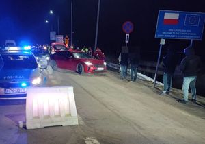 policyjny radiowóz na przejściu granicznym obok stoją ludzie